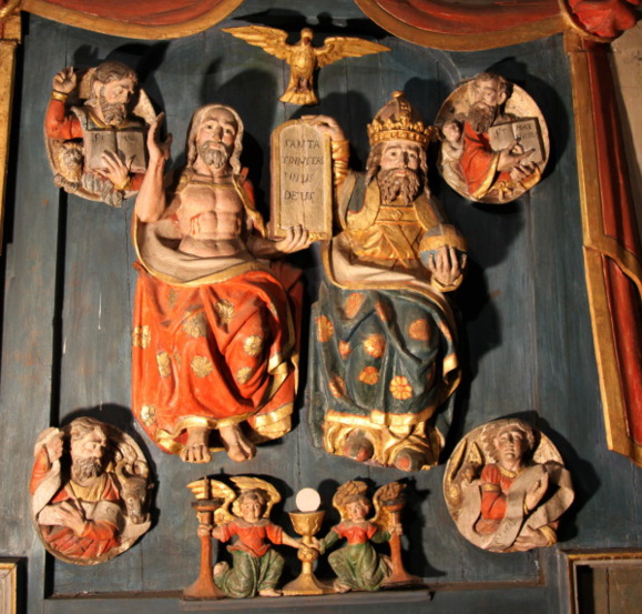 Le retable de la Trinité , XVIe siècle (Église de Saint-Aignan). Sur le fond d'une grande draperie retenue par une couronne, le Père et le Fils, surplombés par l'Esprit-Saint tiennent un tableau en forme d'arche où sont inscrits les mots SANTA TRINITAS UNUS DEUS. Aux quatre coins de cette composition trinitaire, des médaillons présentent les évangélistes et leur attribut : saint Marc et son lion, saint Matthieu et l'ange, saint Luc et le taureau, saint Jean et l'aigle. En dessous, deux anges porteurs de bougeoir présentent le calice et l'hostie de l'Eucharistie. (Crédits photo : Jean-Yves Cordier ) Le retable de la Trinité , XVIe siècle (Église de Saint-Aignan). Sur le fond d'une grande draperie retenue par une couronne, le Père et le Fils, surplombés par l'Esprit-Saint tiennent un tableau en forme d'arche où sont inscrits les mots SANTA TRINITAS UNUS DEUS. Aux quatre coins de cette composition trinitaire, des médaillons présentent les évangélistes et leur attribut : saint Marc et son lion, saint Matthieu et l'ange, saint Luc et le taureau, saint Jean et l'aigle. En dessous, deux anges porteurs de bougeoir présentent le calice et l'hostie de l'Eucharistie. (Crédits photo : Jean-Yves Cordier )